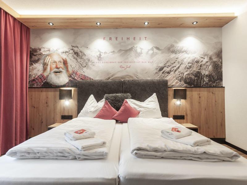 Modern eingerichtetes Hotelzimmer mit zwei Einzelbetten, roter Dekoration und großem Landschaftsbild an der Wand.