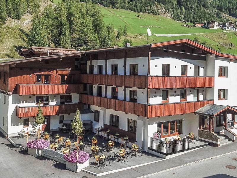 Alpenhotel mit Holzfassade und Terrasse in grüner Berglandschaft
