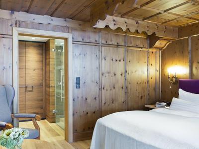 Gemütliches Hotelzimmer mit Holzwänden, Bett und Sesseln neben einer Aufzugstür.