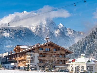 Alpenhotel mit Holzarchitektur vor schneebedeckten Bergen und blauem Himmel.
