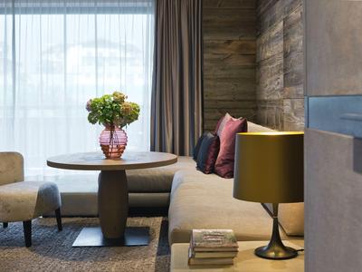 Gemütliche Hotellounge mit Sofa, Sesseln, einem Tisch und dekorativem Blumenstrauß im Fensterlicht.