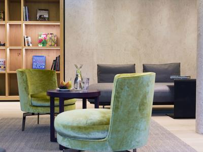 Moderne Hotellounge mit grünen Sesseln, schwarzem Sofa und Holzregal im Hintergrund.