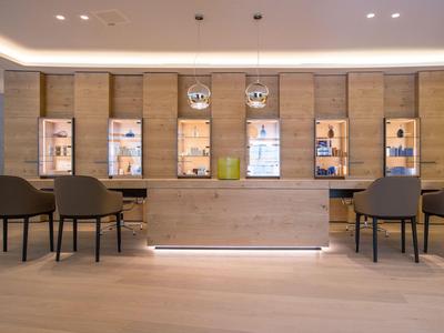 Moderner Hotel-Empfangsbereich mit Holztheke, Stühlen und beleuchteten Regalen im Hintergrund.