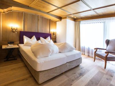 Hell eingerichtetes Hotelzimmer mit großem Bett, Holzvertäfelung und Fenster mit Vorhängen.