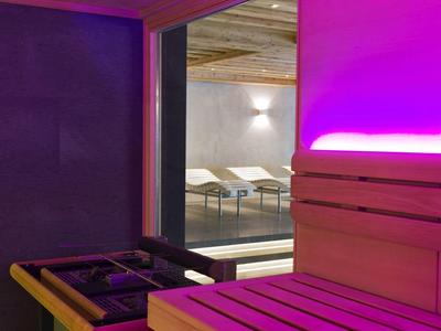 Saunabereich mit Holzbänken und violetter LED-Beleuchtung, Blick auf einen Ruheraum mit Liegestühlen.