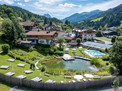 Hotelanlage in den Bergen mit Pool, Liegewiesen und natürlichem Teich, umgeben von Wäldern.