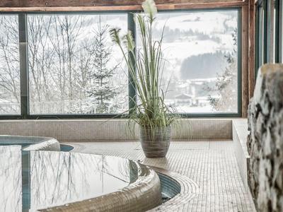 Innenansicht eines Wellnessbereichs mit Pool und großem Fenster zur winterlichen Landschaft