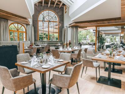 Helles, modernes Restaurant mit Holzmöbeln, großen Fenstern und stilvoll gedeckten Tischen.