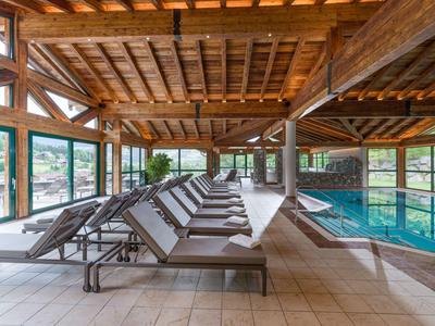 Moderner Hotelpool mit Liegestühlen unter einer Holzgiebeldecke und großen Panoramafenstern.
