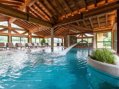 Innenpool mit Wasserfall und Sitzbereich in einem Hotel mit Holzdecke und großen Fenstern.