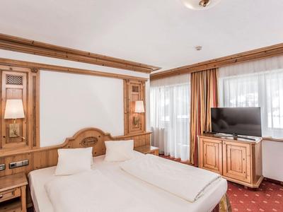 Helles Hotelzimmer mit zwei Betten, Holzvertäfelung und TV vor einem Fenster mit Vorhängen.