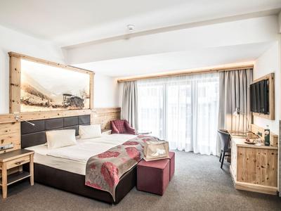 Helles Hotelzimmer mit Doppelbett, Holzvertäfelung und großen Fenstern mit Vorhängen.