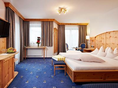 Jasno urządzone pokój hotelowy z drewnianymi meblami, niebieskim dywanem i dwoma łóżkami.