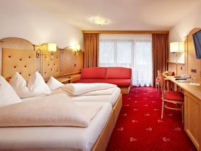 Pokój hotelowy z podwójnym łóżkiem, czerwonym dywanem, sofą i oknami balkonowymi z zasłonami.