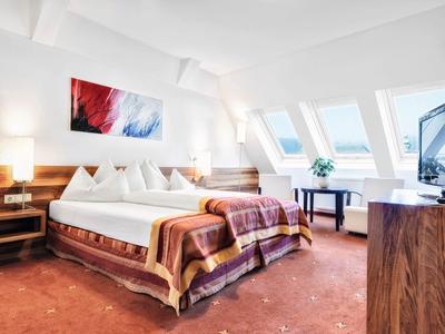 Jasny pokój hotelowy z dużym łóżkiem, kolorowym dywanem i oknami na poddaszu.