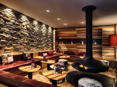 Gemütliches Wohnzimmer mit Steinwand, Holzvertäfelung und zentralem Kaminofen, warm beleuchtet.