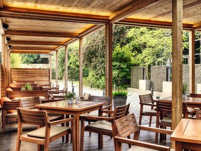 Zadaszona przestrzeń na zewnątrz z drewnianymi stołami i krzesłami w cichym ogrodzie.