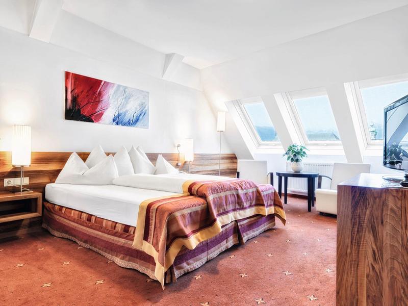 Světlá ložnice s manželskou postelí, dřevěným nábytkem a okny ve střeše.