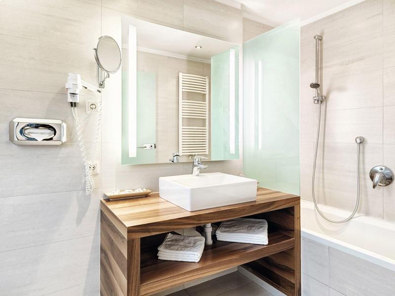 Moderní koupelna se dřevěnou skříňkou, obdélníkovým umyvadlem a vanou se sprchou.