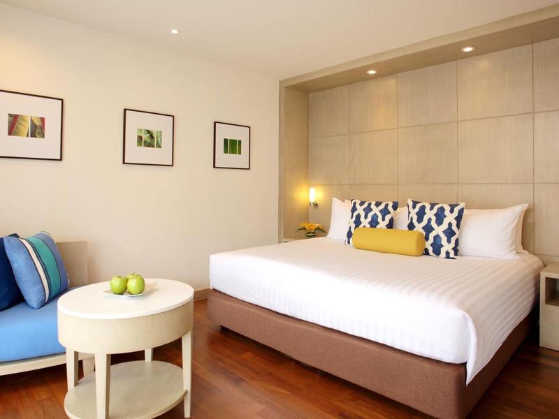 Modernes Schlafzimmer mit großem Bett, bequemer Couch, Holzboden und Wandbildern.