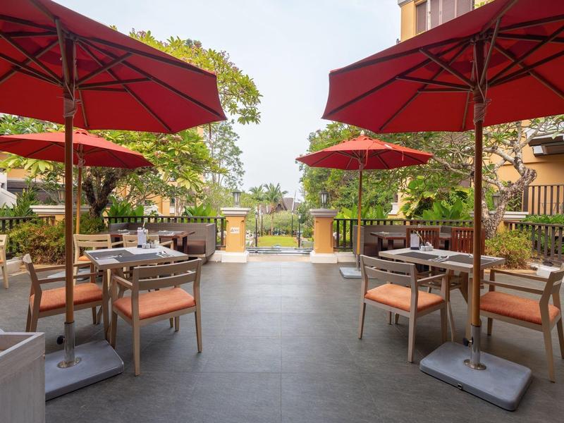 Freiluftrestaurant mit roten Sonnenschirmen, Holztischen und bequemen Stühlen, umgeben von Grün.