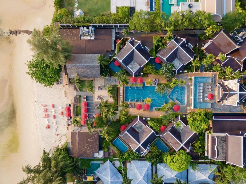 Vogelperspektive eines Resorts am Strand mit Pools, Pavillons und grünen Palmen.