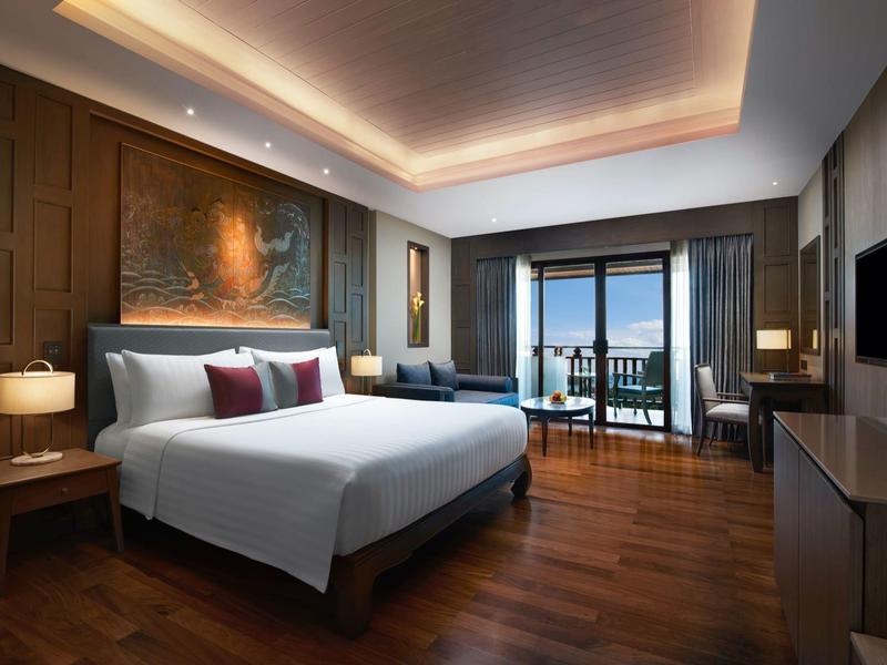 Modernes Hotelzimmer mit großem Doppelbett, Holzboden, bodentiefen Fenstern und Balkon mit Meerblick.