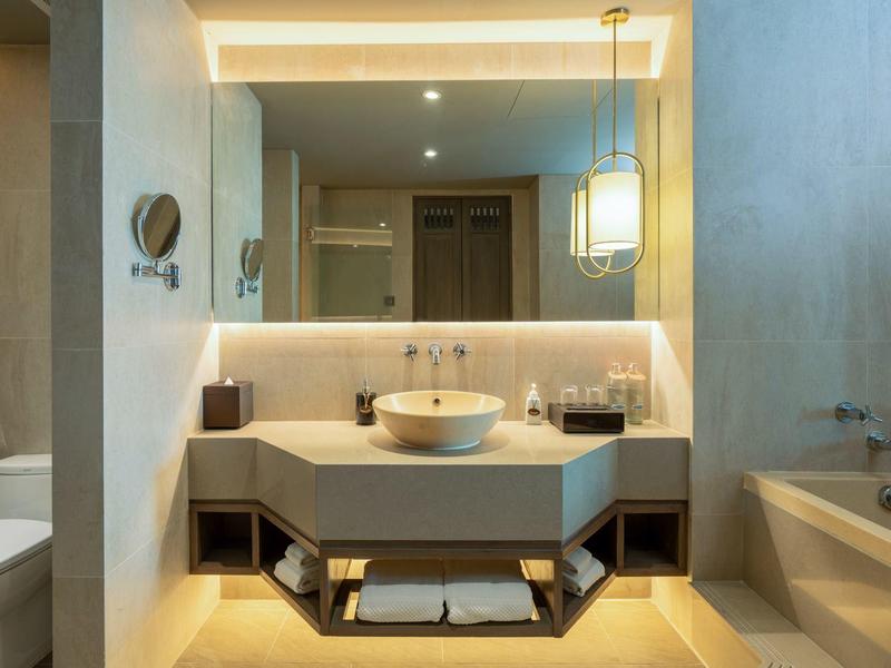 Moderner Badbereich mit weißem Waschbecken, großem Spiegel, Badewanne und Toilettenbereich in neutralen Tönen.