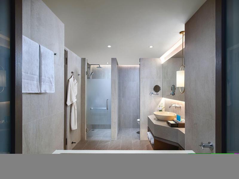 Moderner Hotelbadezimmer mit Dusche, Waschbecken und beigen Fliesen.