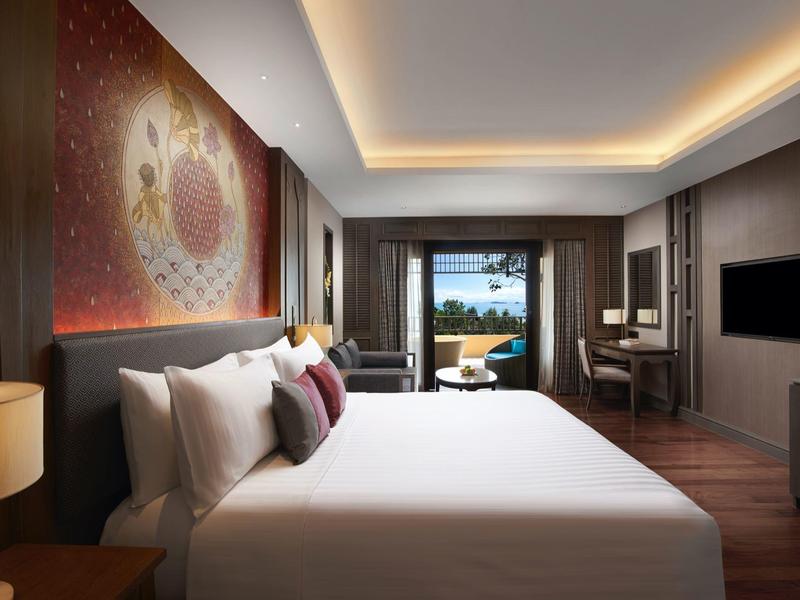 Modern eingerichtetes Hotelzimmer mit großem Bett, Kunst an der Wand und Blick auf Balkon und Meer.