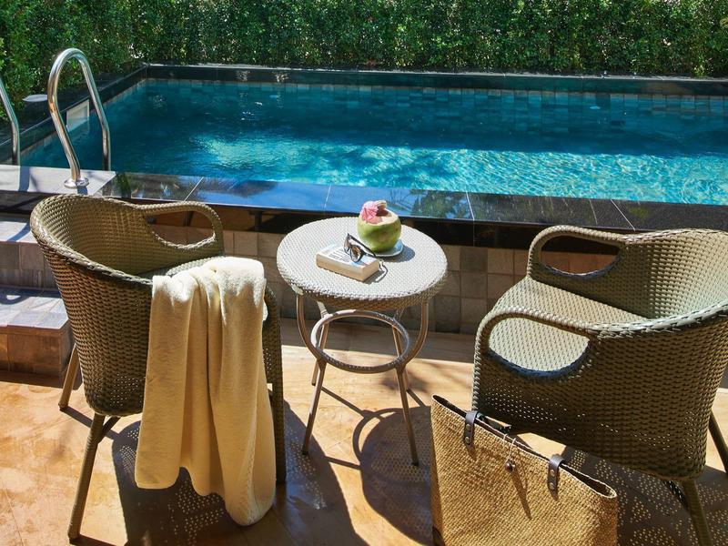 Zwei Stühle mit einem kleinen Tisch dazwischen an einem Pool, mit Handtuch und Tasche.