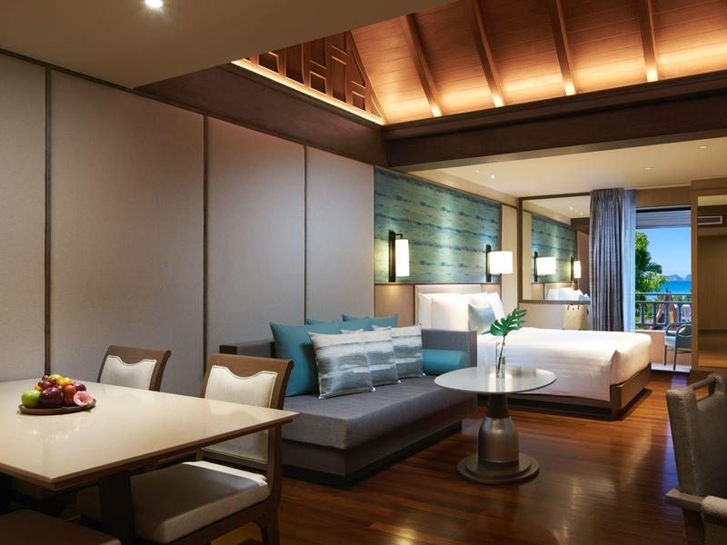 Modern eingerichtetes Hotelzimmer mit Bett, Sofa, Esstisch und Blick auf Balkon.