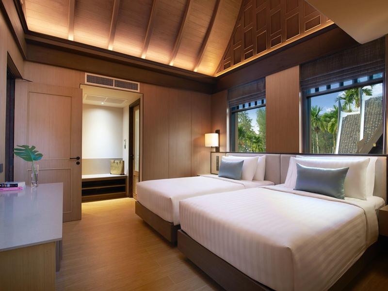 Modernes Hotelzimmer mit großem Bett, warmem Licht und Fensterblick auf grüne Palmen.