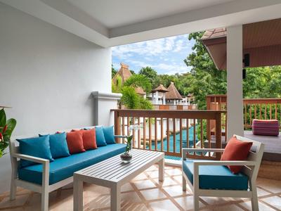 Gemütlicher Balkon mit blauen Sitzmöbeln, Holztisch, Pflanzen und Blick auf Pool und Häuser.
