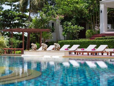 Pool mit klar blauem Wasser und Liegestühlen in einem tropischen Garten mit Palmen.