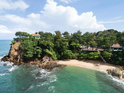 Kleine tropische Bucht mit Sandstrand, Felsen und üppiger Vegetation neben dem Meer.