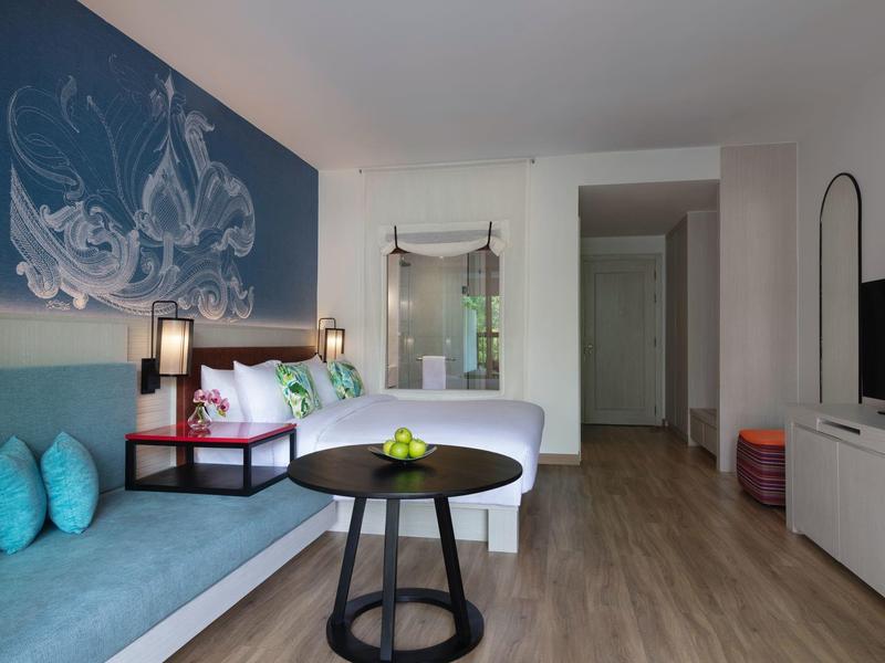 Modernes Hotelzimmer mit Doppelbett, Sofa, rundem Tisch und TV, in hellen Farben und Holzfußboden.