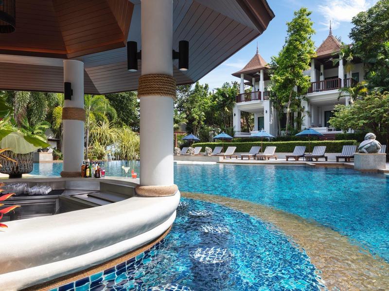 Einladender Pool mit klarem Wasser, Barbereich und tropischer Umgebung mit Palmen und Gebäuden.