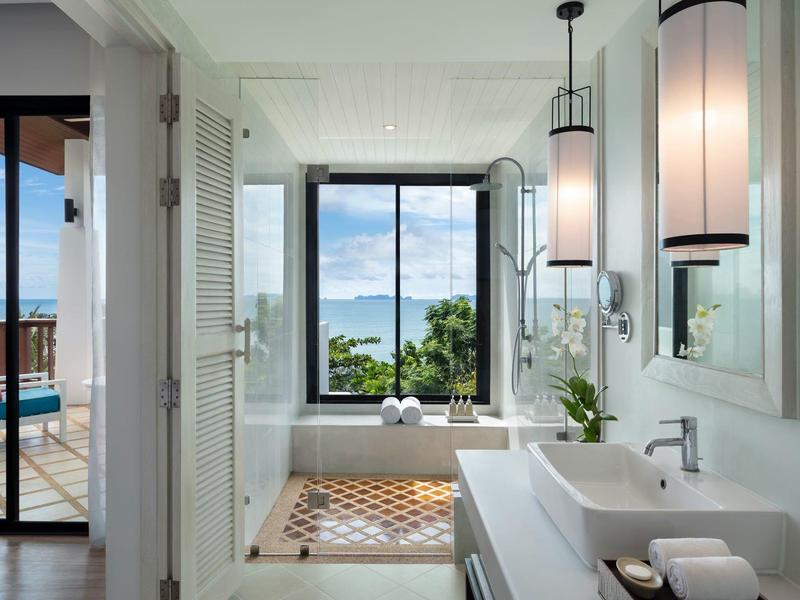 Helles Badezimmer mit großer Glasfront, freistehender Badewanne und Zugang zu Balkon mit Meerblick.