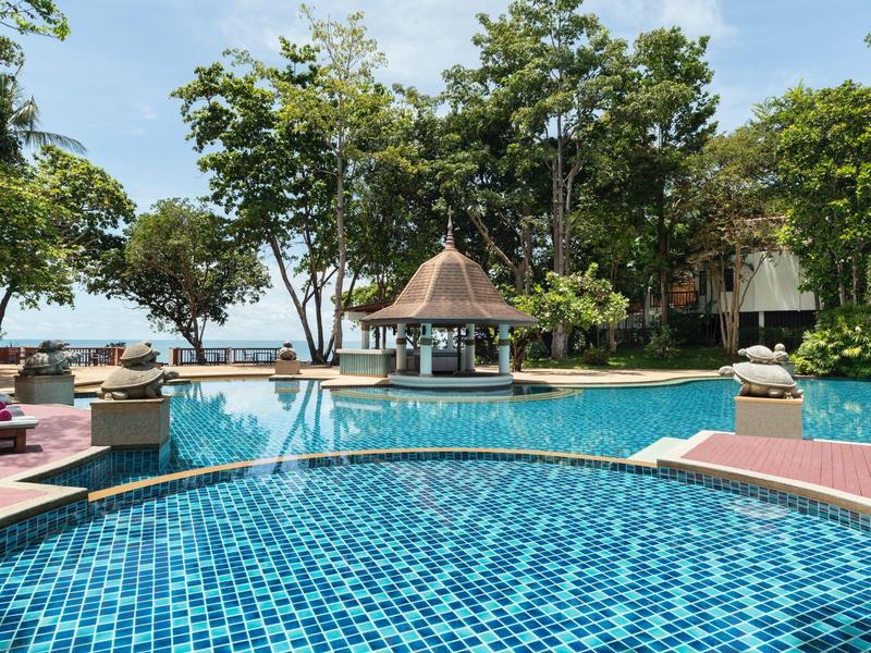 Ein großer blauer Pool mit Liegestühlen und Bäumen in einem tropischen Resort