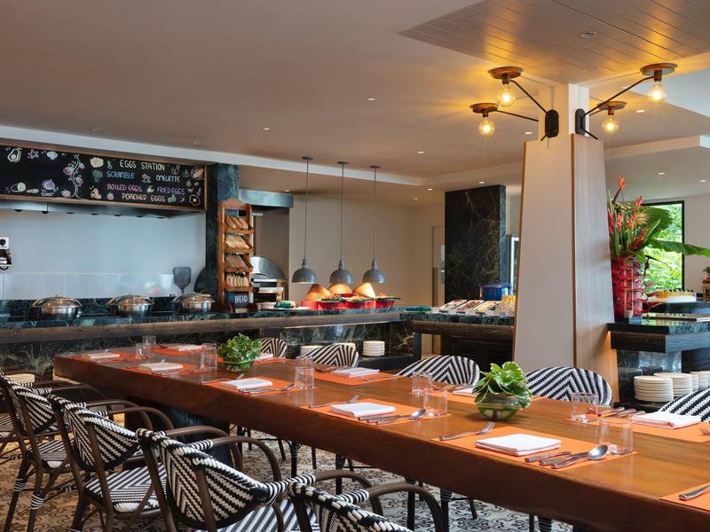 Moderner Essbereich mit Holztischen, schwarzen Stühlen und warmem Licht in einem Hotelrestaurant.
