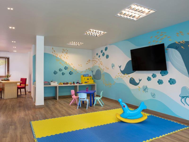 Kinderspielzimmer mit buntem Wal-Wandbild, Spielsachen, buntem Bodenmatten und Fernseher.