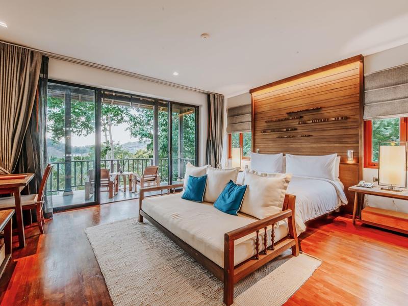 Elegantes Hotelzimmer mit großem Bett, Sofa und Balkon mit Gartenblick.