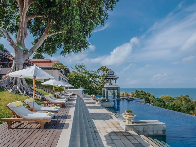 Luxuriöser Poolbereich mit Liegestühlen, Sonnenschirmen und Blick auf das Meer bei sonnigem Himmel.