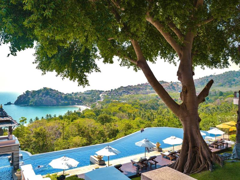 Luxuriöser Infinity-Pool mit weißen Sonnenschirmen vor Meer und grüner Küstenlandschaft.