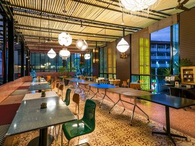 Moderne Hotelbar mit langen Tischen, Stühlen und warmem Licht am Abend.