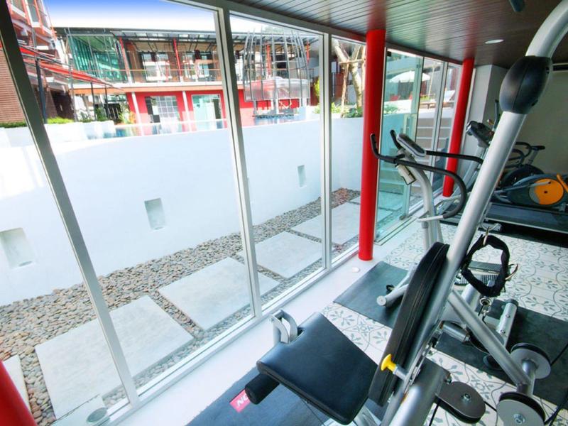 Fitnessraum mit großen Fenstern, Blick auf Innenhof, Hantelbank und Trainingsgeräte, helle Atmosphäre.