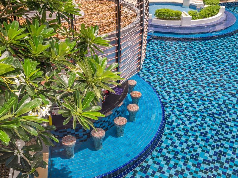 Blauer Mosaikpool mit Wasserspielen und grünen Pflanzen in einem runden Areal.