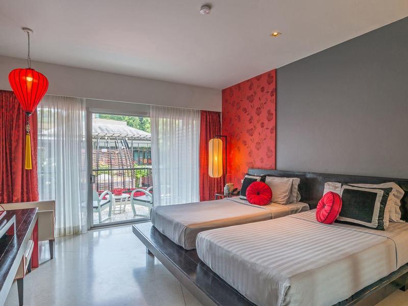 Modernes Hotelzimmer mit zwei Betten, roten Akzenten, grauer Wand und Balkon mit Blick nach draußen.