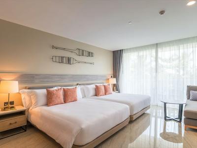 Moderner Hotelzimmer mit zwei großen Betten, Sitzbereich und großen Fenstern mit Vorhängen.